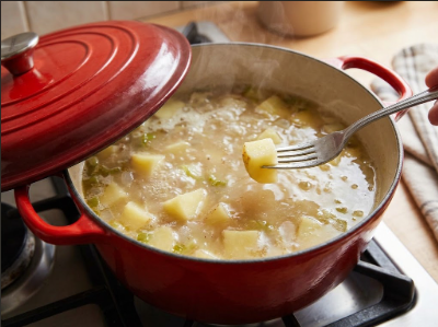 Dutch oven of simmering broth and potato cubes, lid ajar, with a fork piercing one cube
