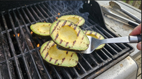 Spatula lifting an avocado half to show char marks on the cut side