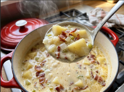 A ladle lifting thick, creamy potato soup from the pot, showing potato chunks and flecks of bacon
