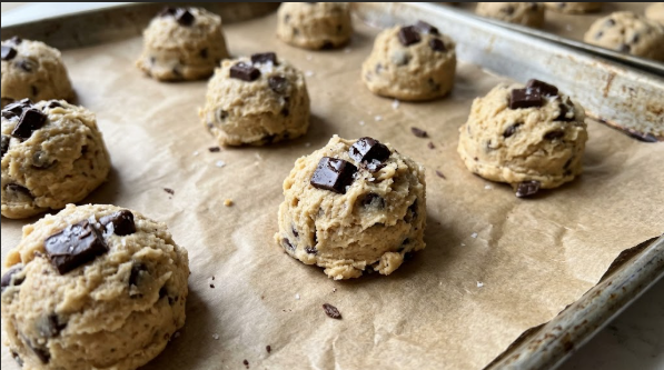 Dough balls on the lined sheet, spaced apart, with extra chocolate pressed on top