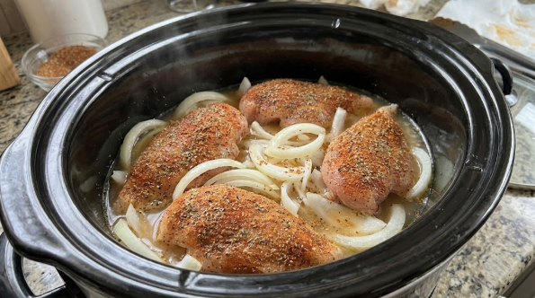  Seasoned chicken breasts resting in a single layer on sliced onions in the slow cooker, with ½ cup of broth in the bottom]