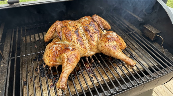 Spatchcocked chicken laid flat on a pellet grill grate, skin golden and brushed with butter