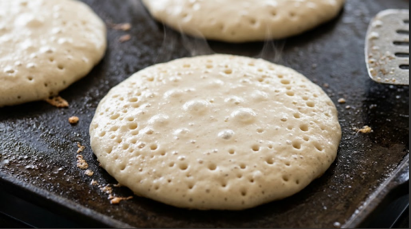 pancakes on the griddle showing bubbles across the surface right before flipping