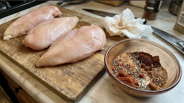 Raw chicken breasts patted dry on a cutting board, with the spice rub in a small bowl beside them