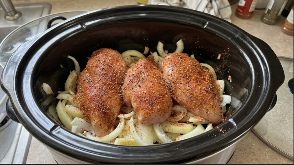  Seasoned chicken resting on a bed of sliced onions inside the slow cooker before the lid goes on