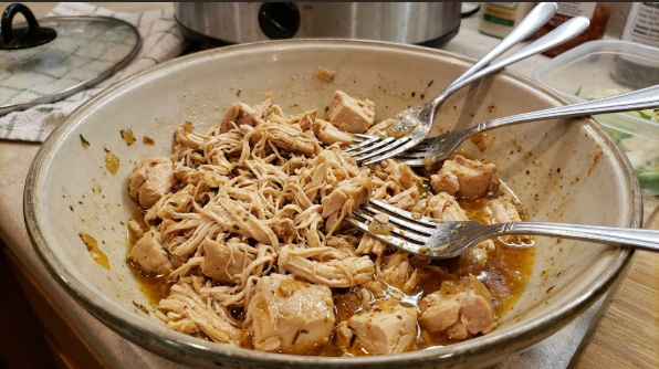  Shredded crockpot chicken in a bowl with two forks, glistening with cooking juices