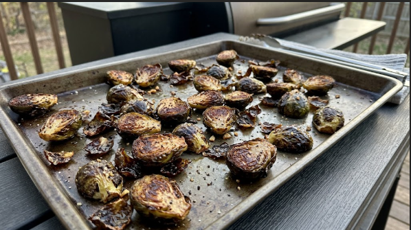 Halved Brussels sprouts on a sheet pan with crispy, dark edges, just off the pellet grill