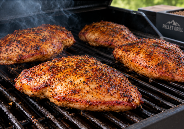 Smoked chicken breasts on a pellet grill grate, deep golden-brown with a light smoke ring at the edge