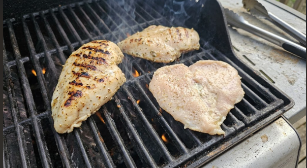 Marinated chicken breasts laid on hot grates showing initial grill marks