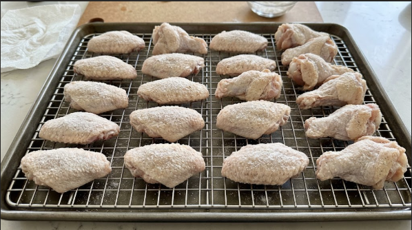 Raw wings spread on a wire rack, dried and coated with a thin, even layer of baking powder and salt