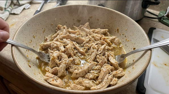 Shredded crockpot chicken breast tossed in cooking juices in a bowl