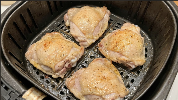 Thighs skin-side down in the air fryer basket after the first 12 minutes, showing rendered fat and light color