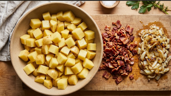 Cubed Yukon Gold potatoes in a bowl next to crisp chopped bacon and sautéed onions