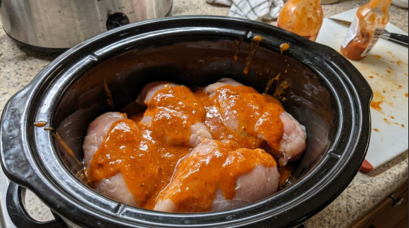Raw chicken breasts in the slow cooker with the buffalo sauce poured over them