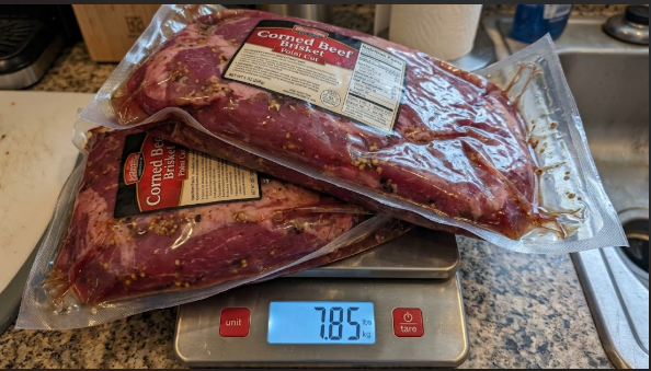 Two raw corned beef briskets in their packages on a scale, showing the raw weight