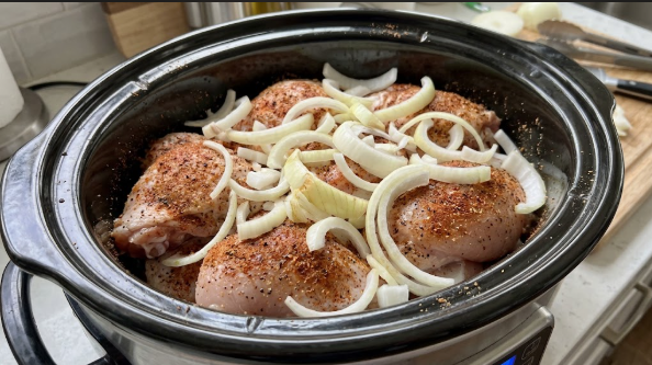 Raw chicken breasts and thighs in the slow cooker, seasoned with the dry rub and topped with sliced onion