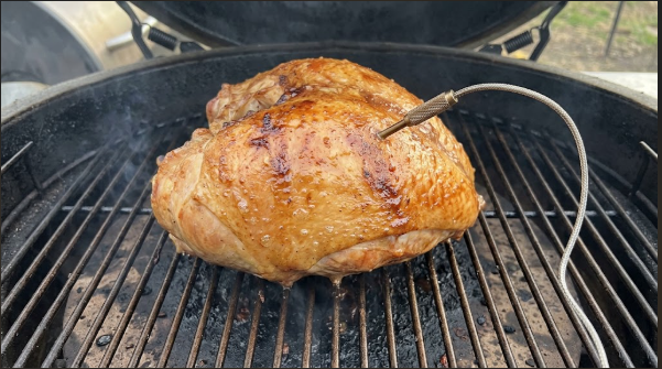Turkey breast on the pellet grill grate with a probe in the thickest part, skin turning amber