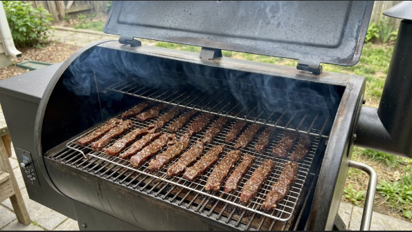  Jerky racks on the grill grate with thin blue smoke coming out of the vent