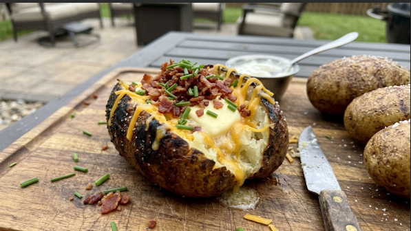 Split grilled baked potato with melting butter, cheddar, bacon, and chives