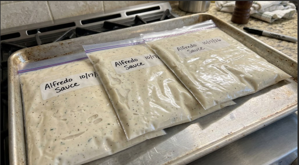Alfredo sauce portioned into flat zip-top bags, labeled and lying on a baking sheet