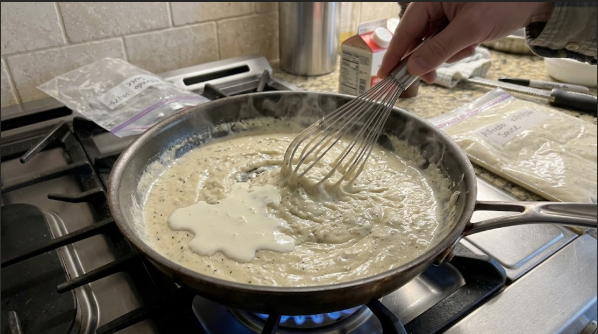 Thawed Alfredo being whisked in a skillet over low heat with a splash of cream