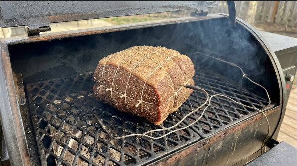 Seasoned roast on the pellet grill grate with the probe inserted