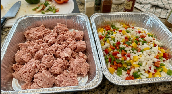 Raw ground turkey crumbled into an aluminum pan next to a second pan of diced onions and peppers