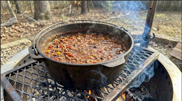 Dutch oven of chili simmering on the grate with a thin wisp of blue smoke