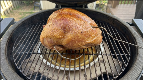 Turkey breast on the kamado grate over a drip pan, skin golden, thermometer probe in place