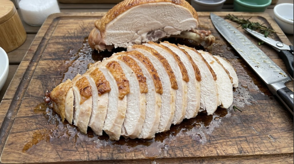 Sliced turkey breast fanned out on a cutting board, skin on top, juices visible