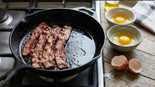  Bacon strips sizzling on the left zone with a thin sheen of fat pushed to the cooler side
